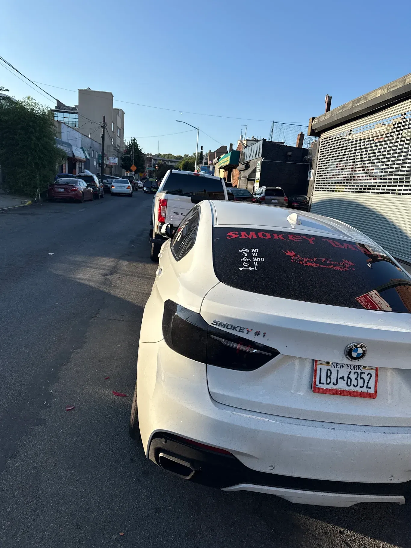 White BMW parked on city street, other cars and buildings in background.