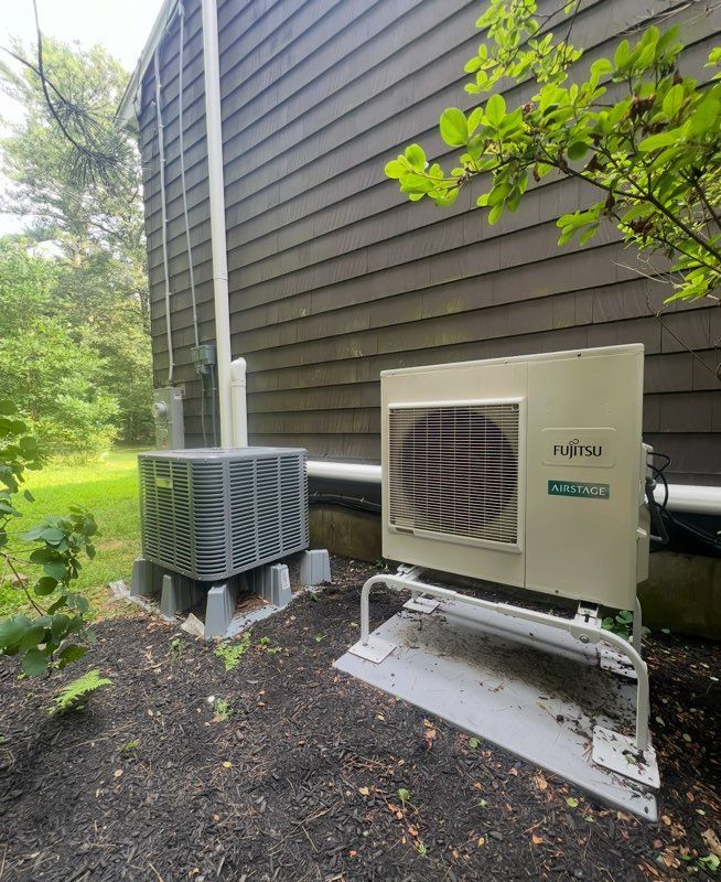 An outdoor air conditioning unit mounted on the yellow exterior wall of a building above a fence.