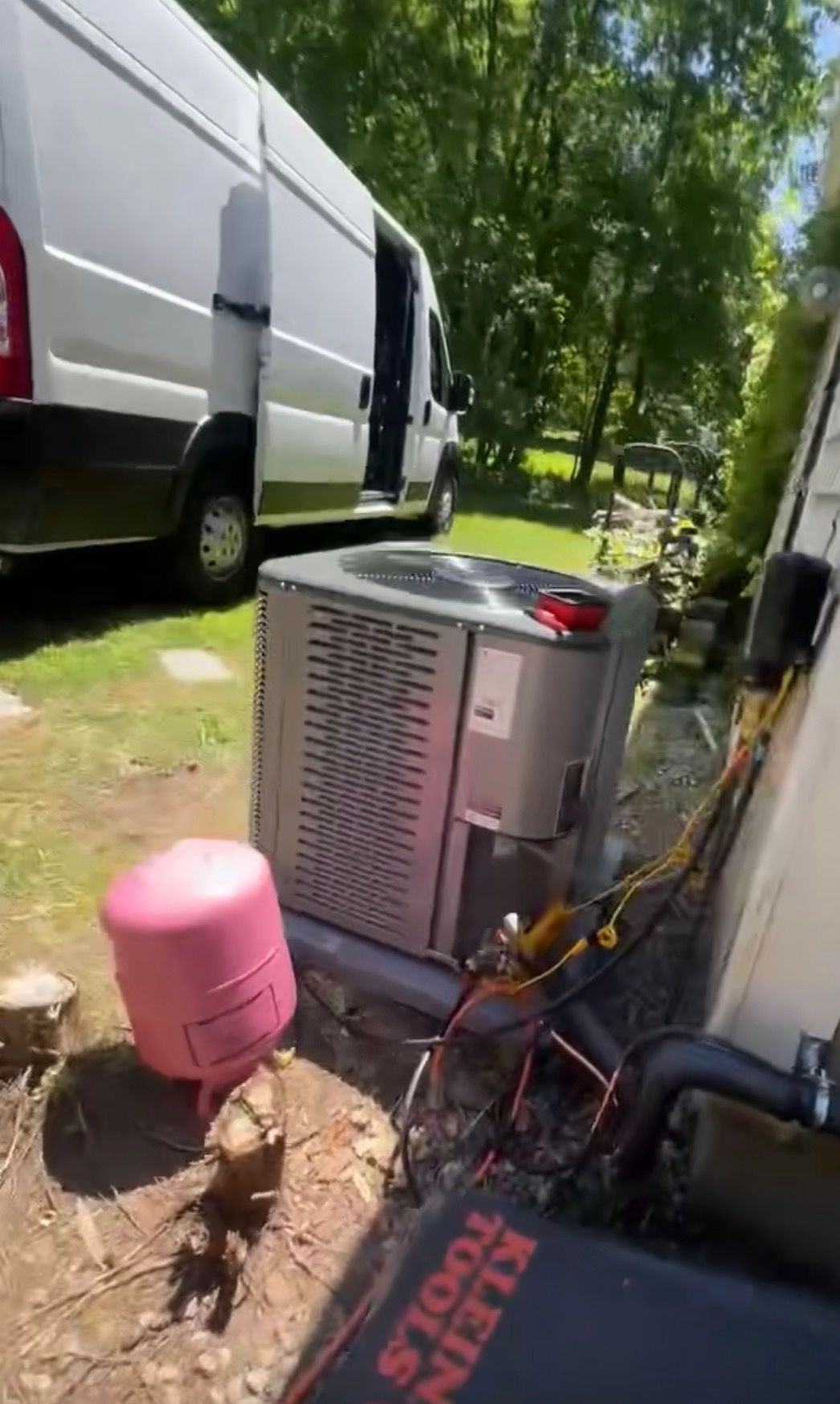 An HVAC technician’s van parked on a lawn next to an outdoor air conditioning unit being serviced with tools nearby.
