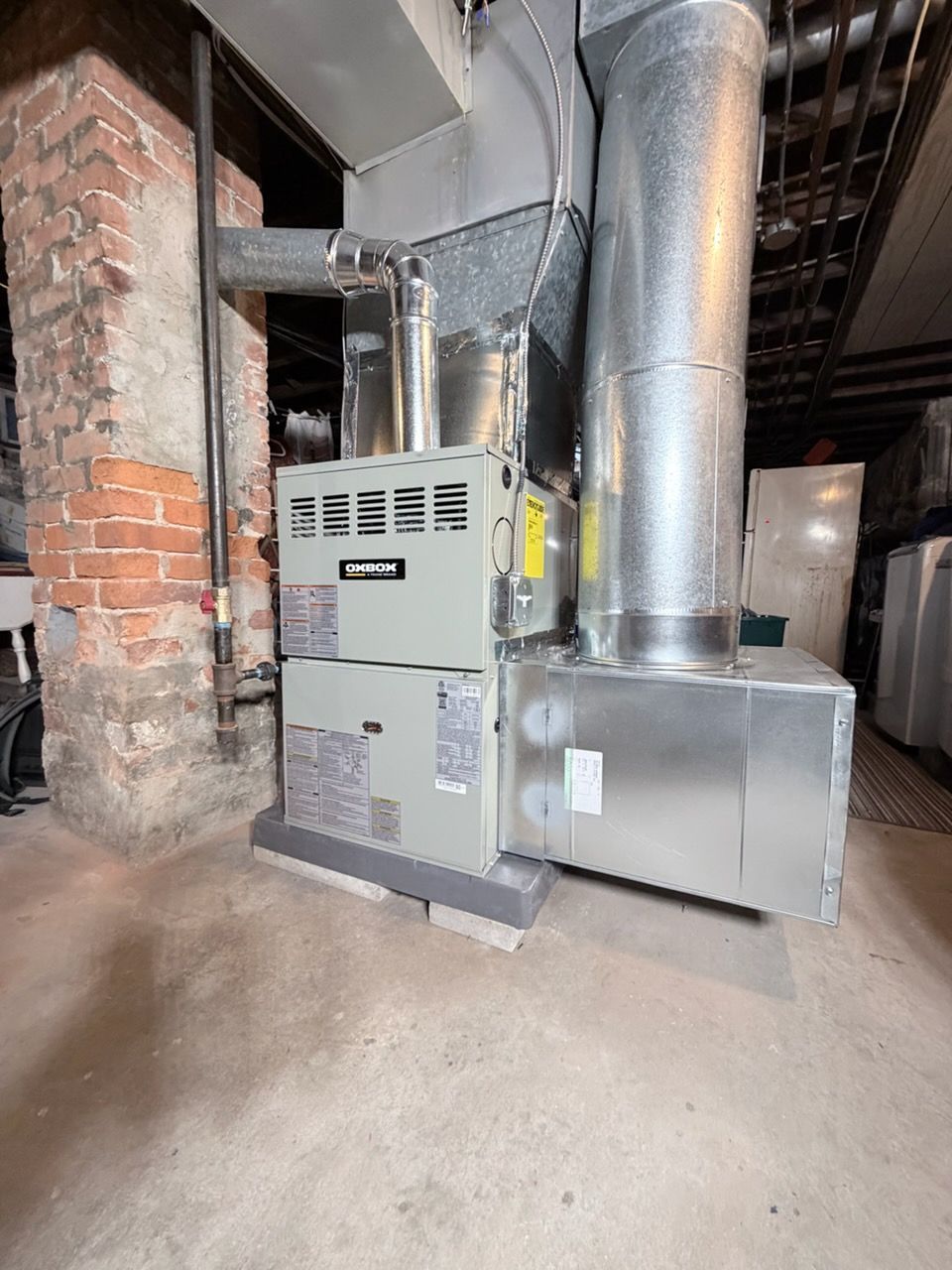 A gray residential water heater tank stands in a basement corner next to silver insulation and white louvered doors.