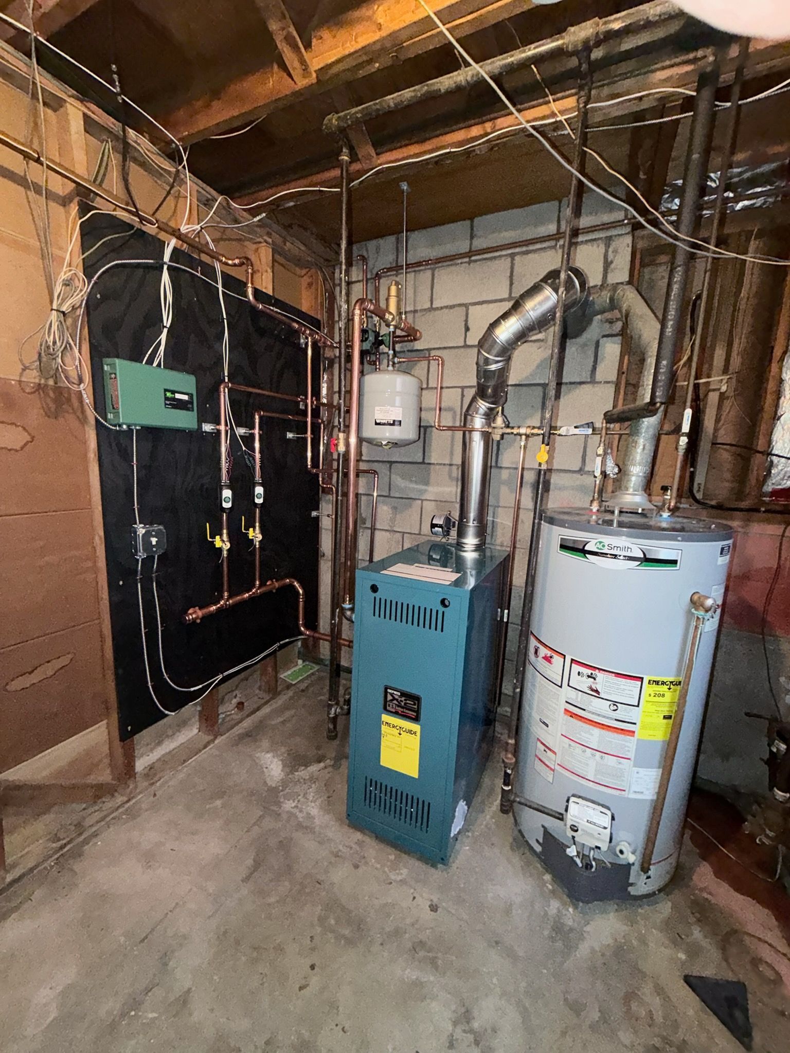 Two HVAC units on gravel pads installed against the exterior wall of a house with beige siding and two basement windows.