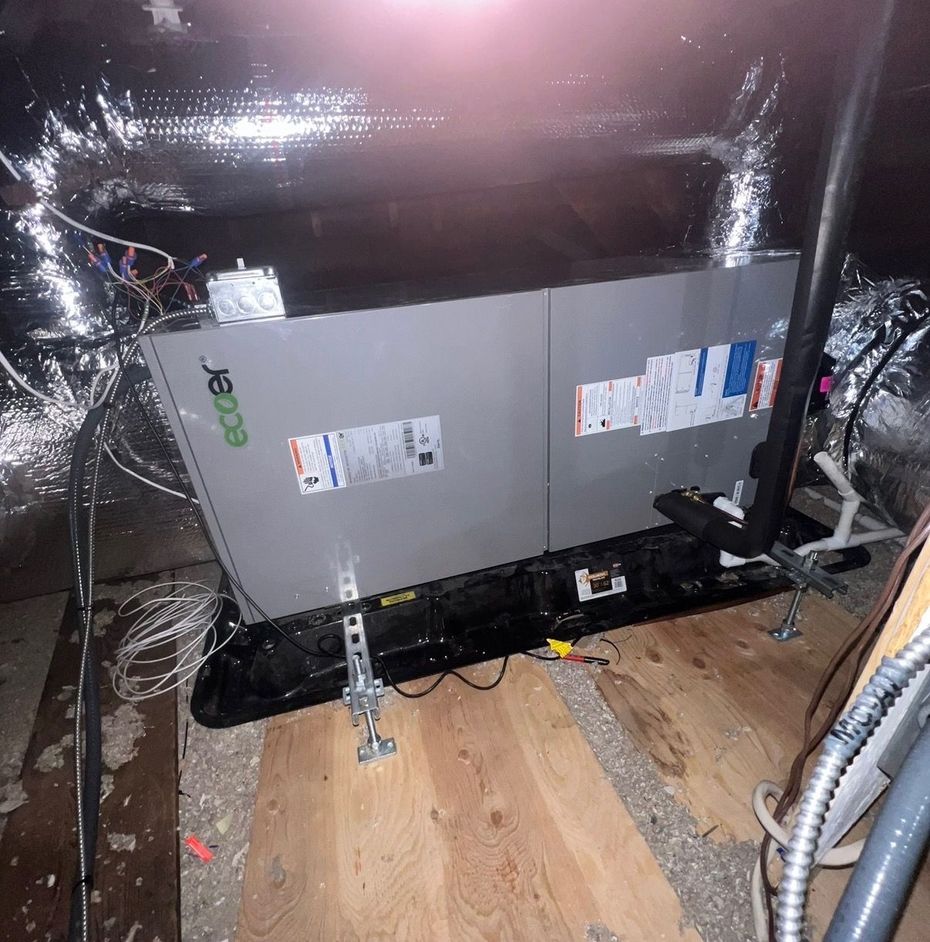 A white air conditioning condenser unit mounted on the exterior yellow wall of a building above a fence.