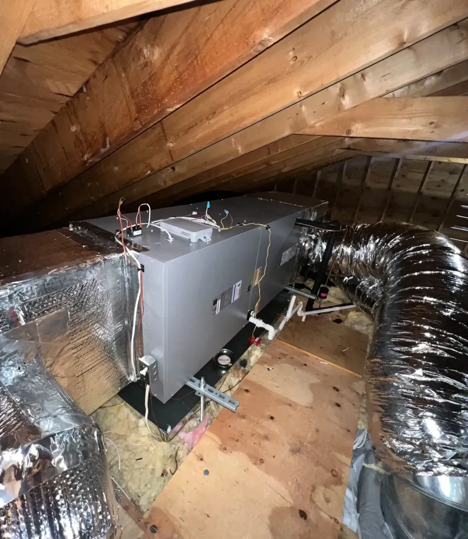 An HVAC air handler unit installed in an attic with attached metal and flexible insulated ductwork.