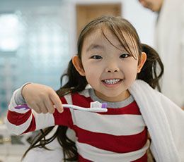 Un enfant souriant, vêtu d'un t-shirt à rayures rouges et blanches, tenant une brosse à dents avec du dentifrice dessus.