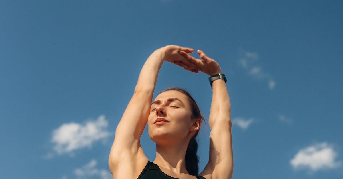 Une personne lève les bras au-dessus de sa tête, se détachant sur un ciel bleu clair parsemé de nuages ​​blancs, les yeux fermés en signe de détente.