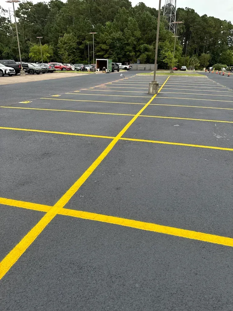 An empty parking lot with bright yellow painted lines marking rectangular parking spaces under a clear sky.