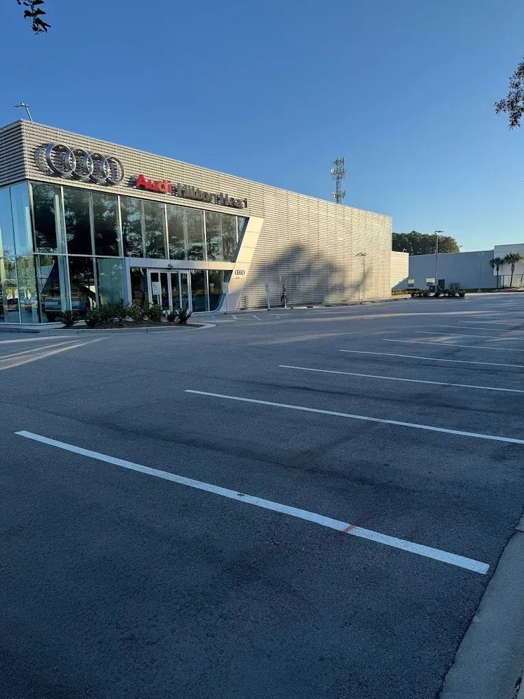 An Audi dealership building with large glass windows and gray textured walls, situated next to an empty parking lot.