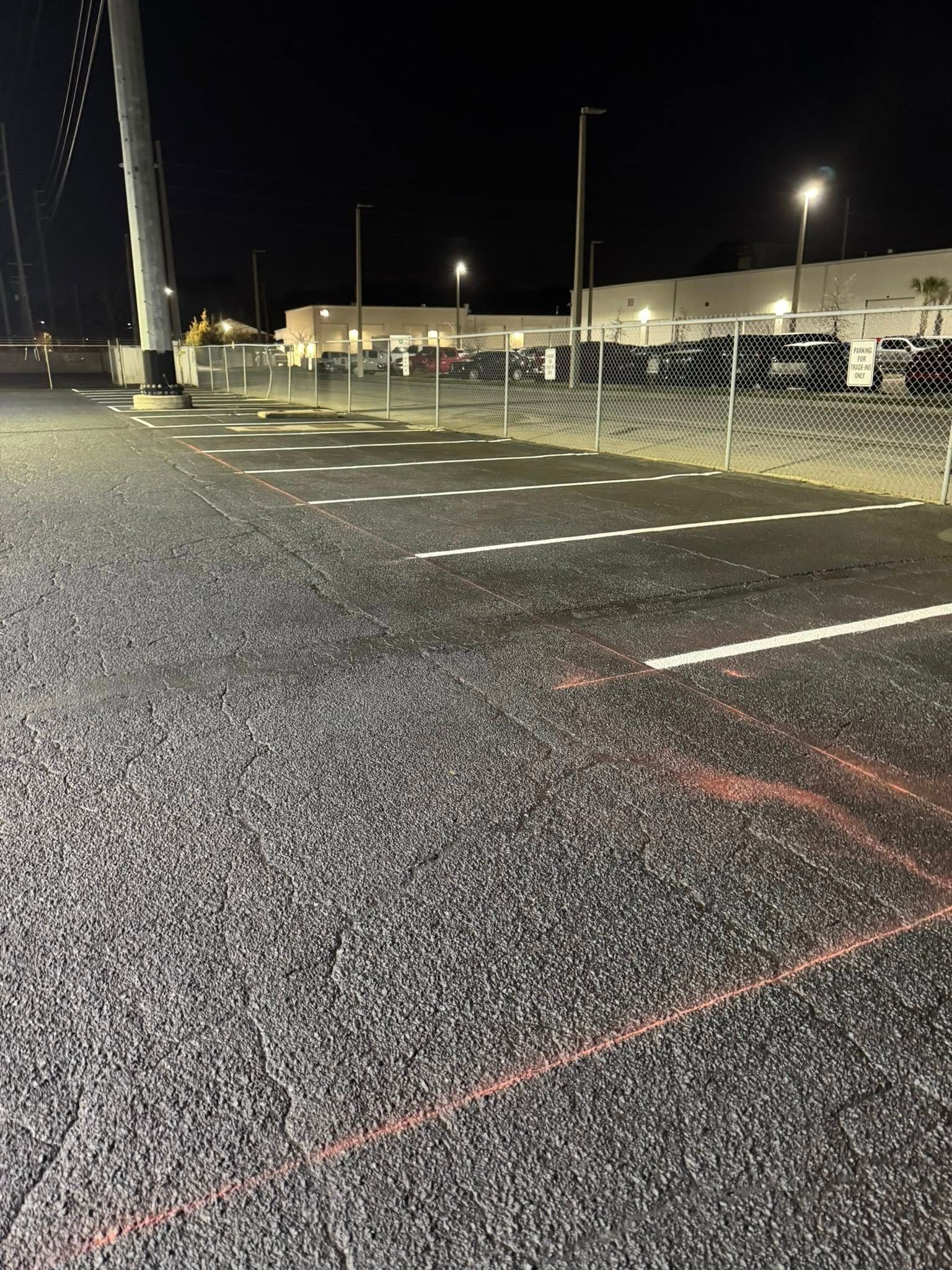An outdoor parking lot at night with painted white parking lines and orange utility markings on the asphalt.