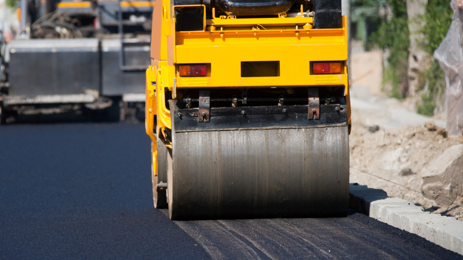 A yellow road roller compacting freshly laid black asphalt on a road construction site.
