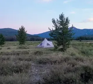 A tent is sitting in the middle of a field with mountains in the background.