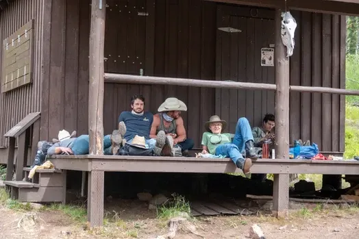 A group of people are sitting on a porch of a wooden cabin.