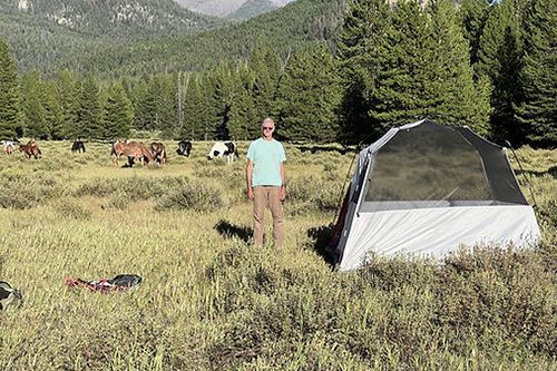 A man is standing in a field next to a tent.