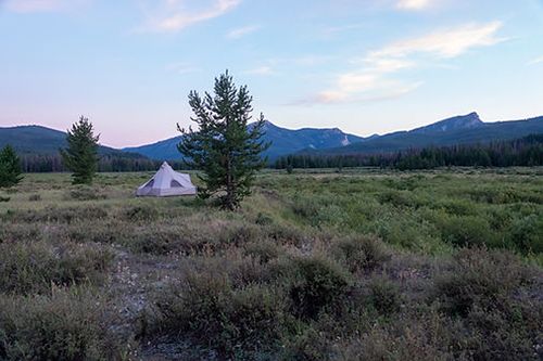 A tent is sitting in the middle of a field with mountains in the background.