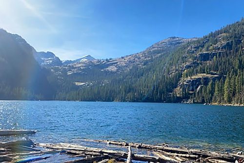 A lake surrounded by mountains and trees on a sunny day