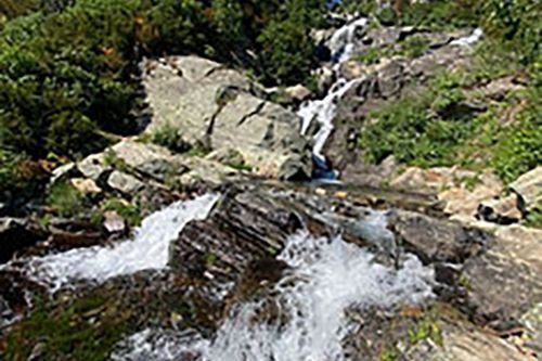 A waterfall is surrounded by rocks and trees in the mountains.