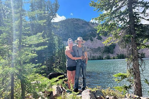 A man and a woman are standing next to a lake in the woods.