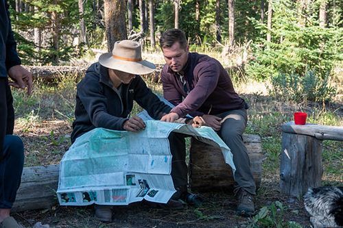 Two men are sitting on a bench in the woods looking at a map.