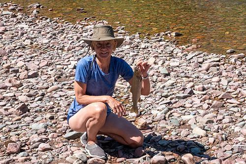 A woman is kneeling on a rocky beach holding a fish.