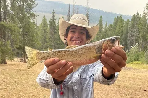 A man in a cowboy hat is holding a fish in his hands.