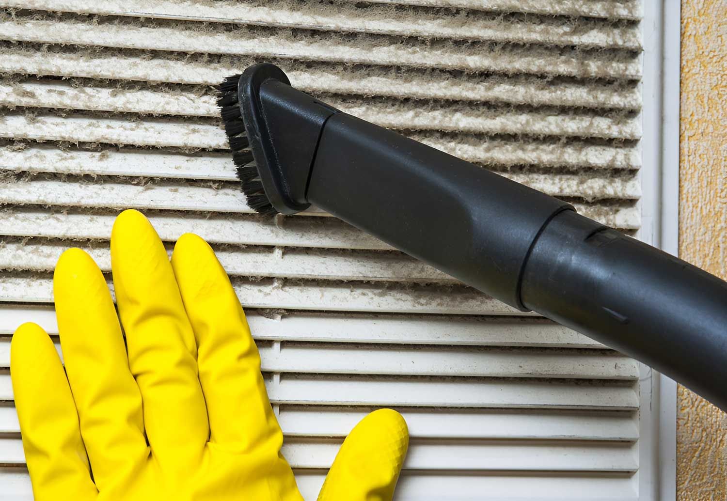 A Person Wearing Yellow Gloves Is Cleaning A Vent With A Vacuum Cleaner — Dryology Carpet Cleaning in Mayfield, NSW