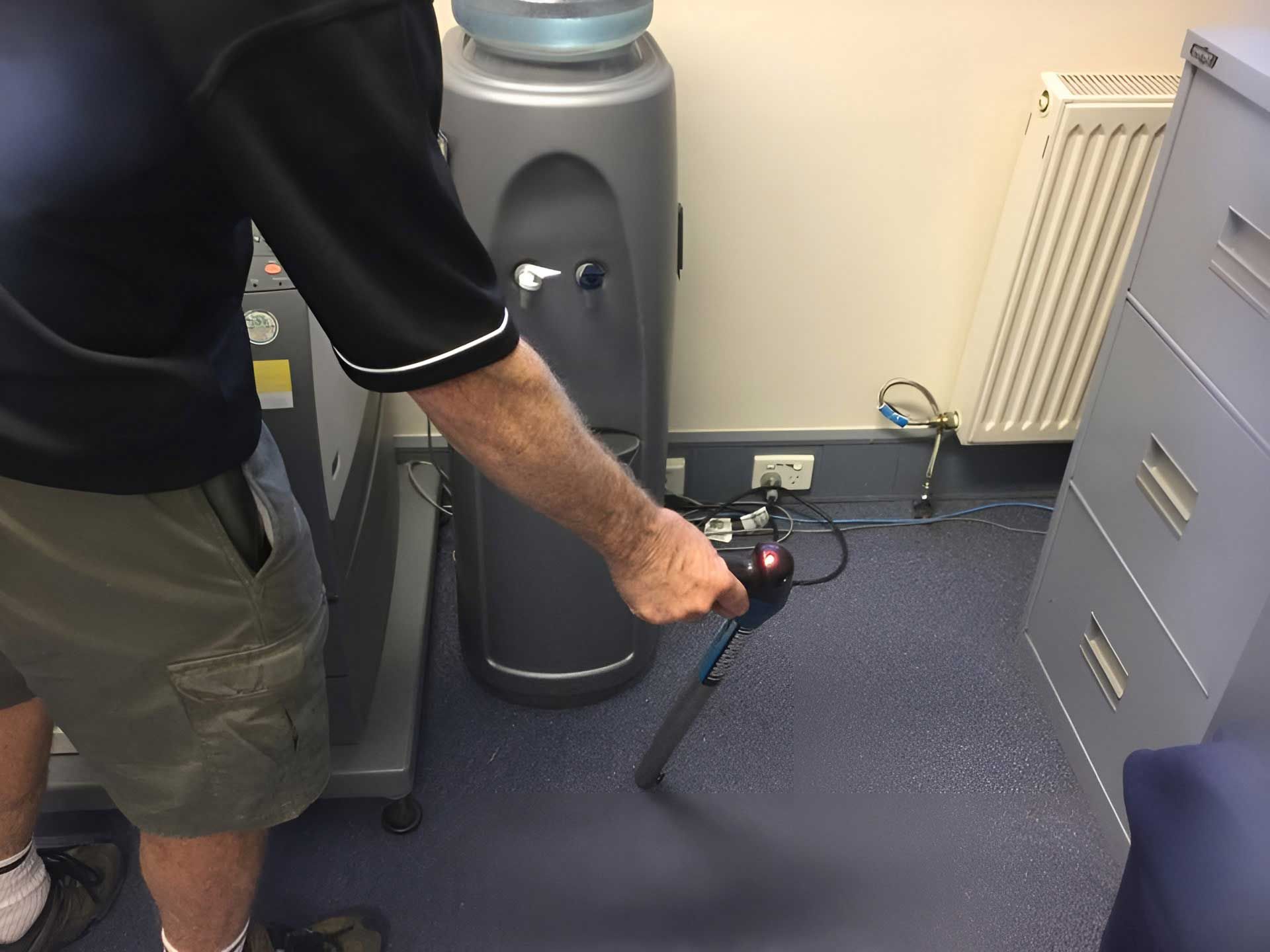 A Man is Holding a Vacuum Cleaner in Front of a Water Cooler β Dryology Carpet Cleaning in Salamander Bay, NSW