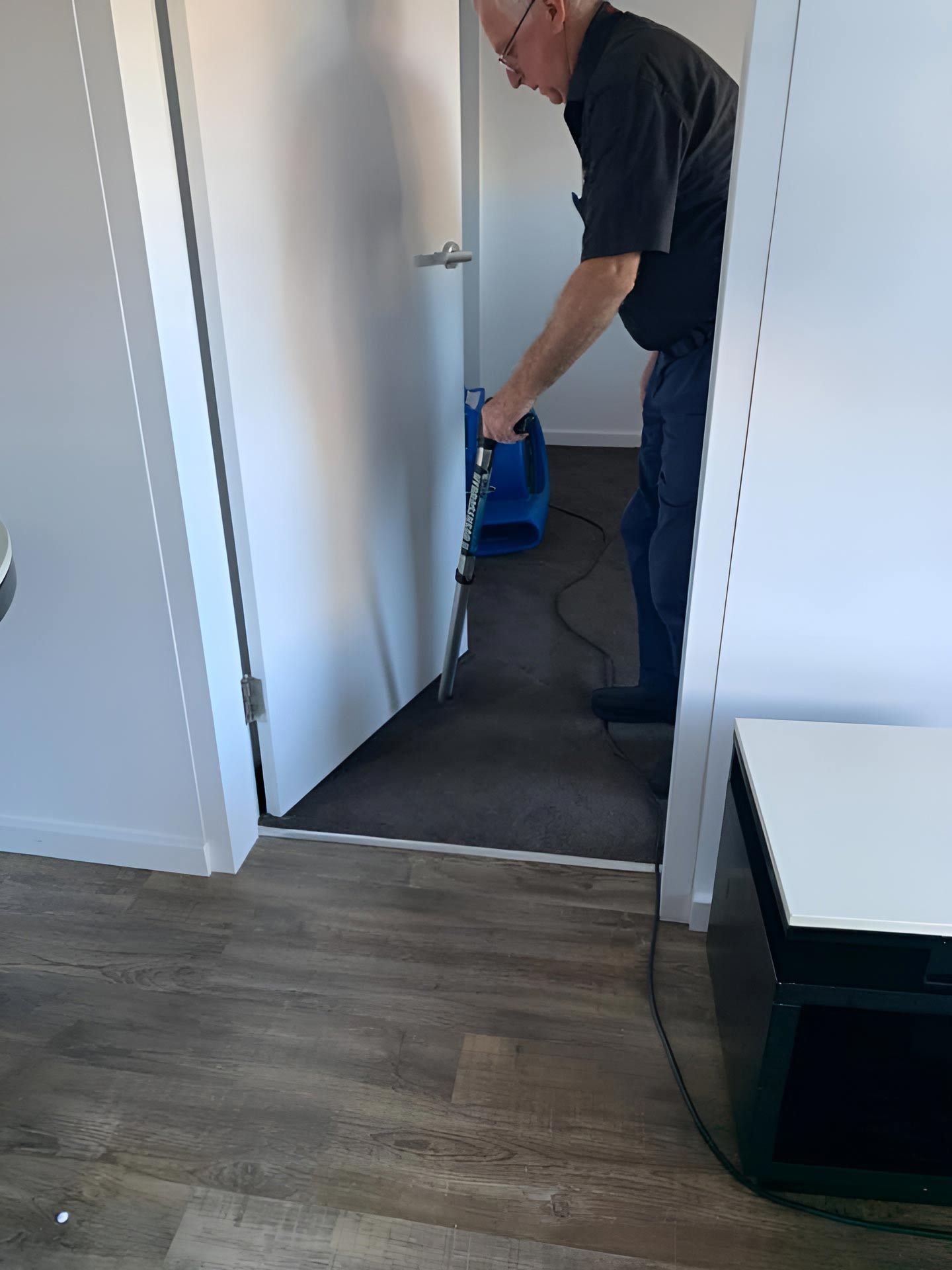 A Man Is Using A Vacuum Cleaner To Clean The Floor In A Room — Dryology Carpet Cleaning in Belmont, NSW