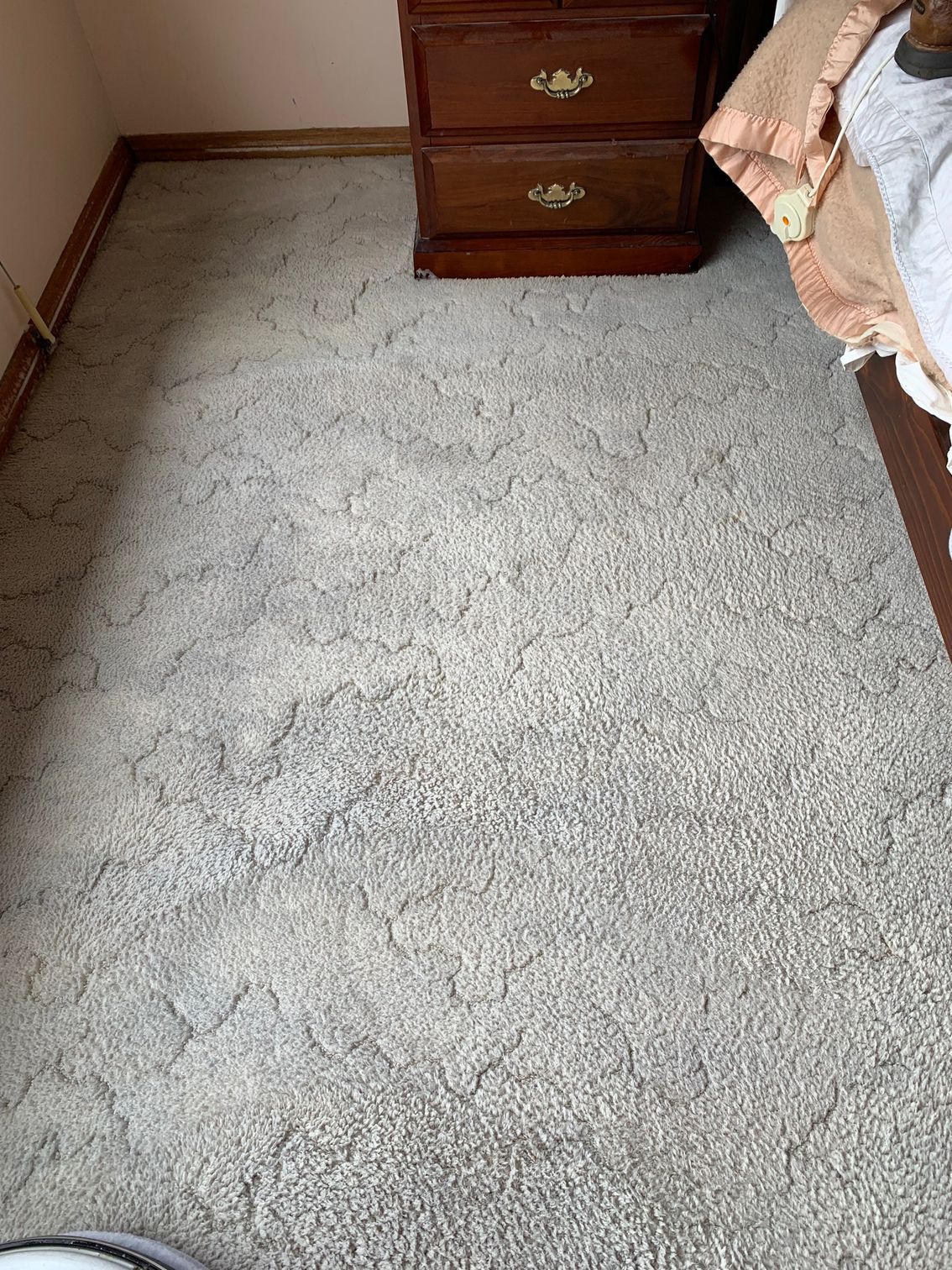 A room with a gray carpet and a wooden nightstand. A bed is partially visible on the right.