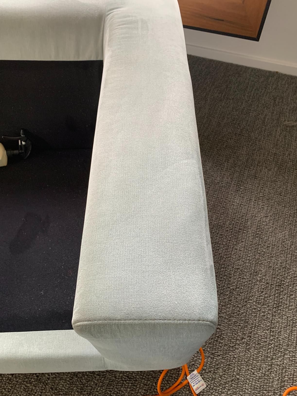 Light gray upholstered sofa arm on gray carpet, with an orange cord visible — Dryology Carpet Cleaning in Salamander Bay, NSW