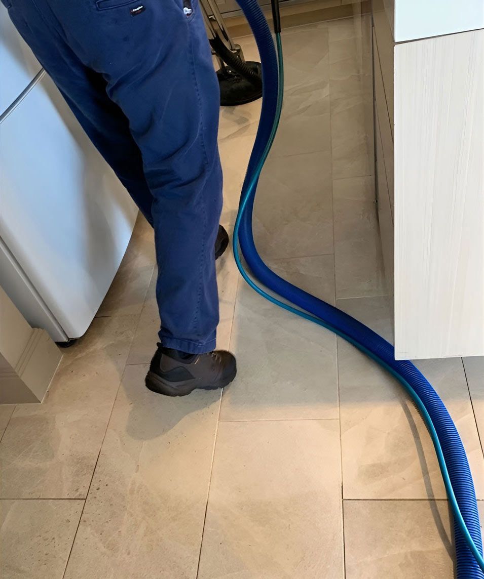 A Person Standing Next To A Blue Vacuum Hose On A Tiled Floor — Dryology Carpet Cleaning in Maitland, NSW