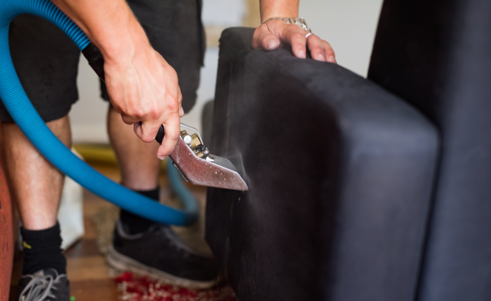 Person using a vacuum nozzle to clean a dark blue upholstered armchair indoors.