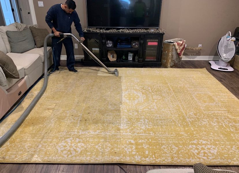 A man is cleaning a yellow rug with a vacuum cleaner in a living room.