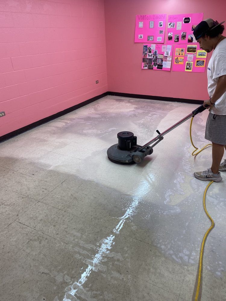 A man is cleaning the floor with a machine in a room with pink walls.