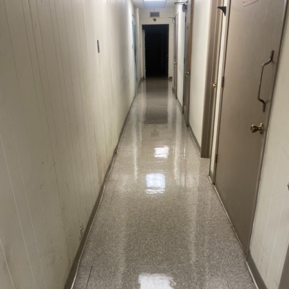 Narrow, empty hallway with white panel walls, glossy floor, and closed doors.