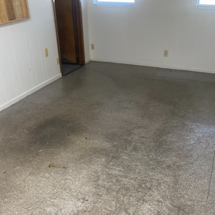A concrete floor in a room with white walls, a brown door, and small windows.