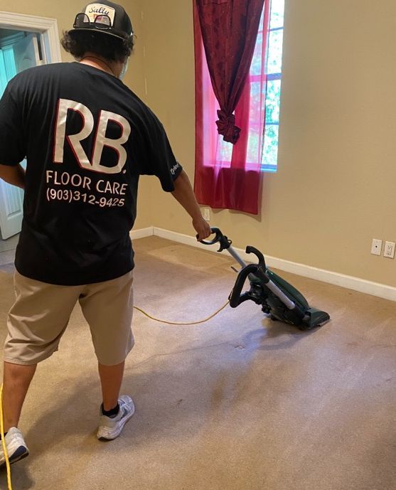 A person in a black shirt vacuums a carpeted room with a machine.