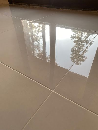 Shiny, light-colored tiled floor reflecting a window with trees and sky outside.