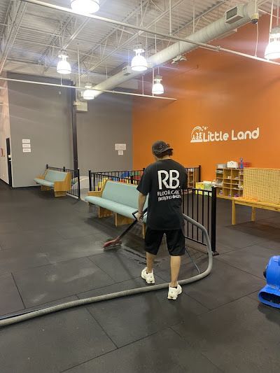 Man vacuuming the floor in a children's play area with orange and gray walls, benches, and play equipment.