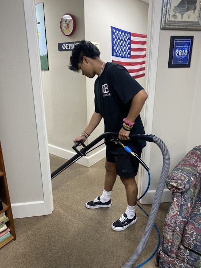 Young person cleaning a carpet with a vacuum in a room with an American flag.