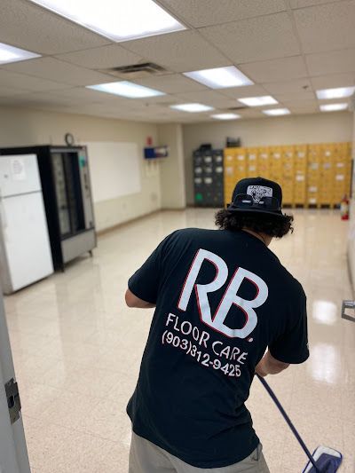 Person with a black shirt cleaning a shiny floor in a room with lockers and a vending machine.