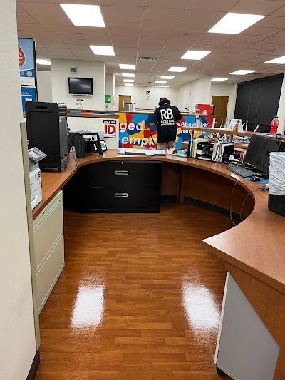 Reception area with curved desk, person standing behind it. Brown wood floors and counter.