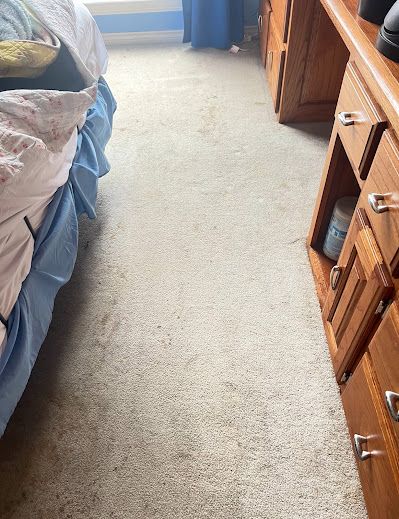 Beige carpet in a bedroom, between a bed and a wooden dresser.