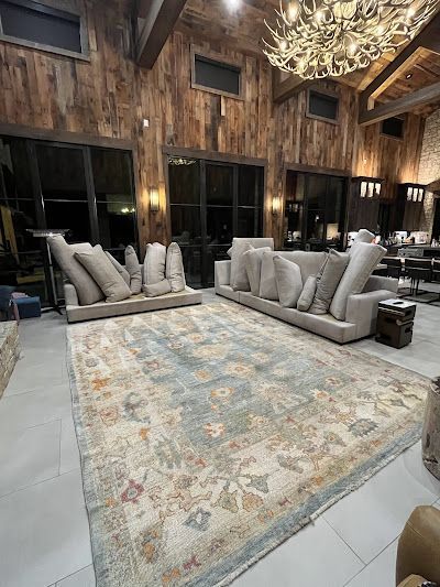 Spacious living room with light blue rug, two sofas, and wooden walls. Antler chandelier hangs overhead.