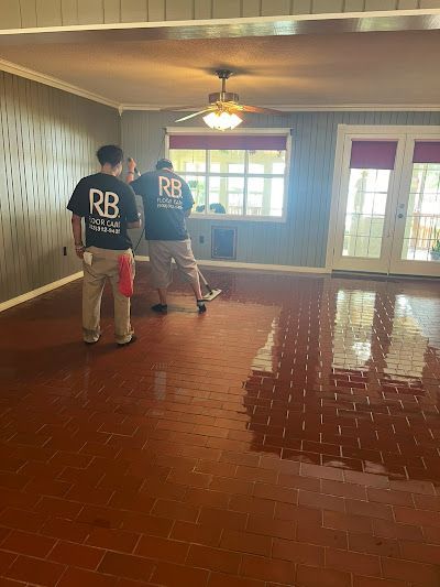 Two people in matching shirts are working on a wet, red-stained floor inside a room.