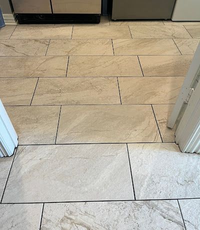 Beige rectangular tiles on a kitchen floor; a doorway and appliances are visible.