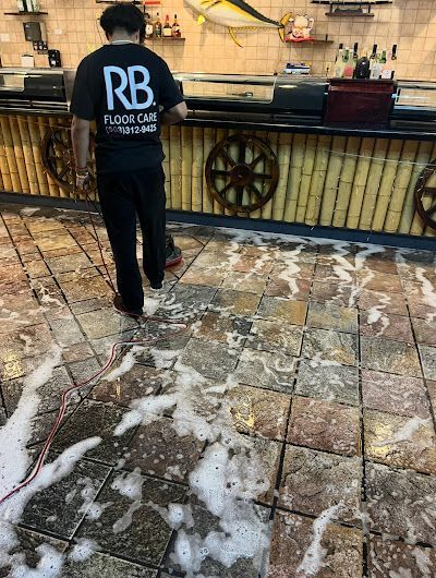 Man cleaning a restaurant floor with soapy water; setting is at a sushi bar.