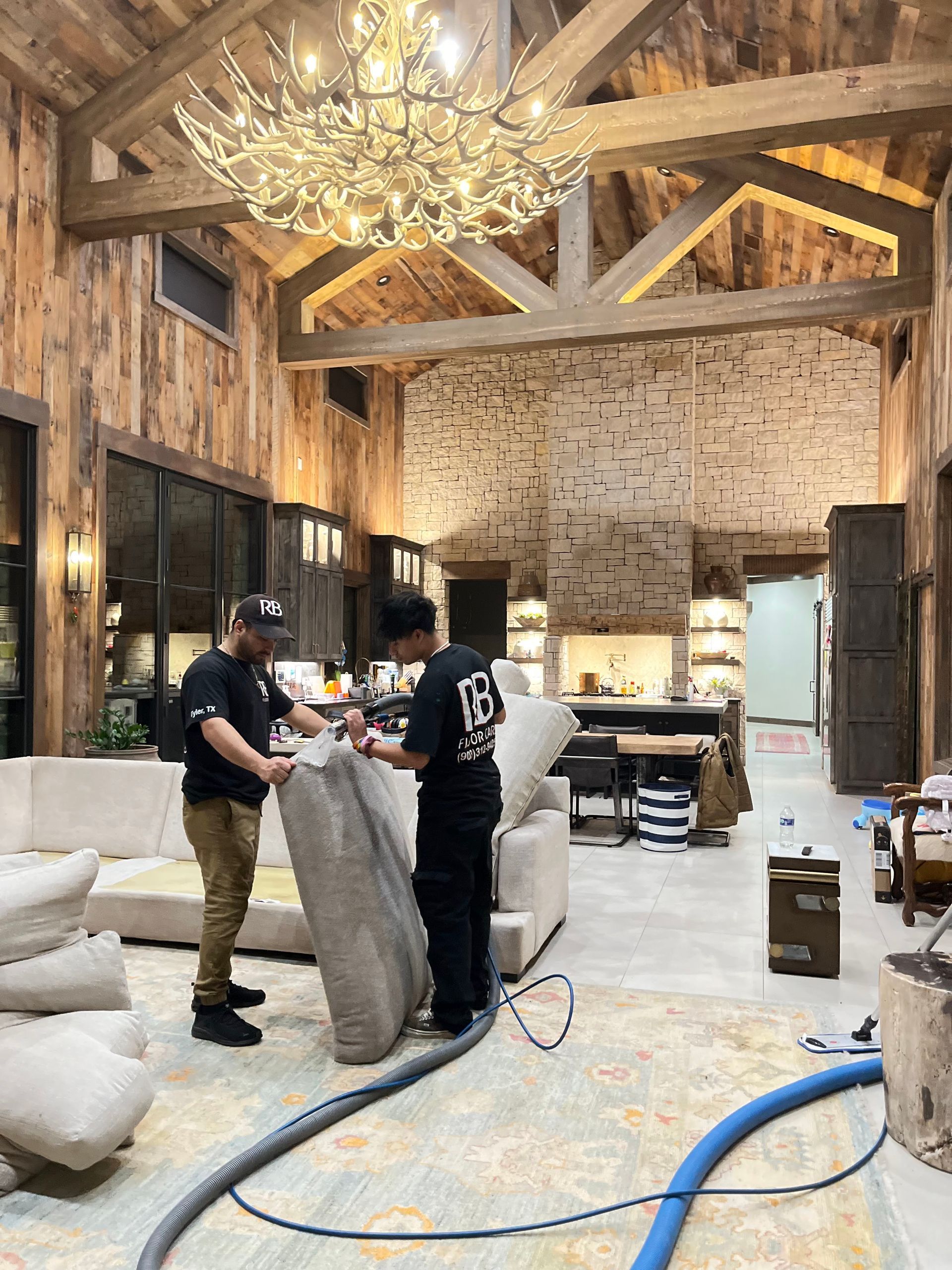 Two men are cleaning a couch in a living room.