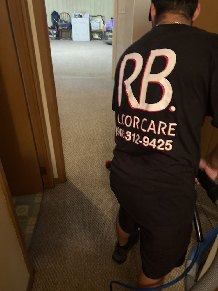 Man cleaning carpet in a doorway, wearing a black shirt with 