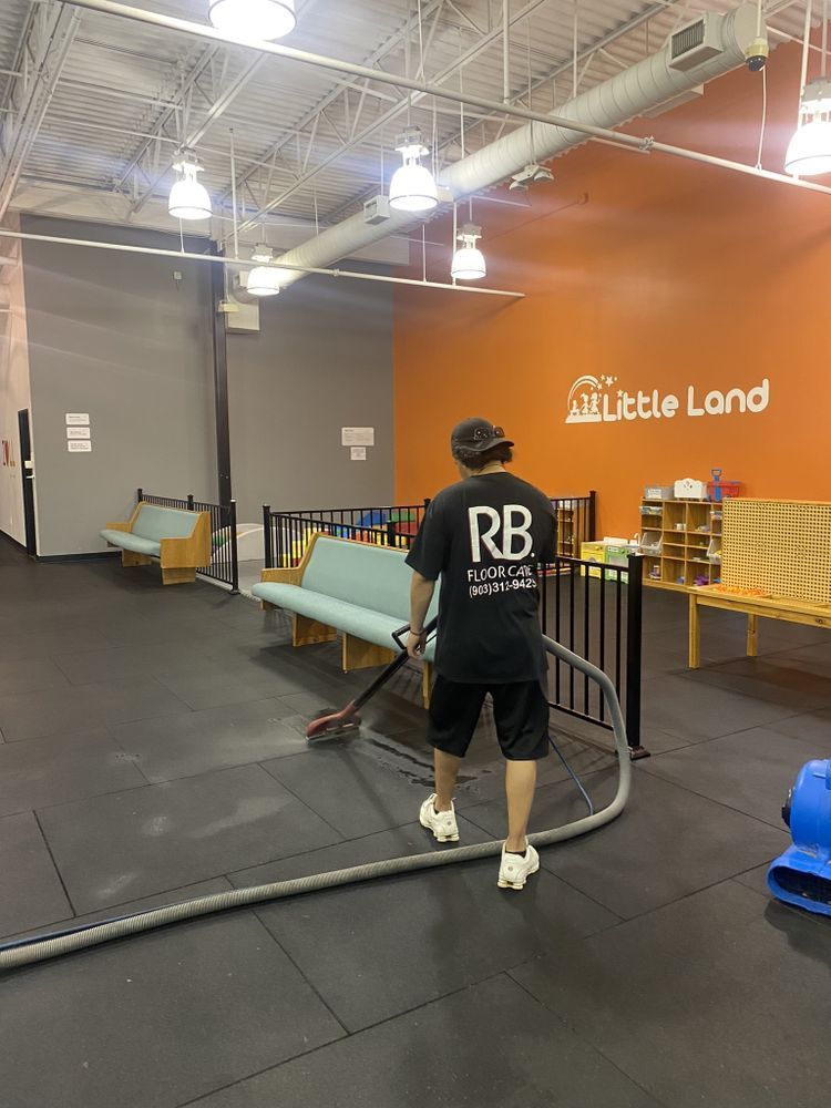 A person vacuuming a black floor in a children's play area with orange and gray walls.
