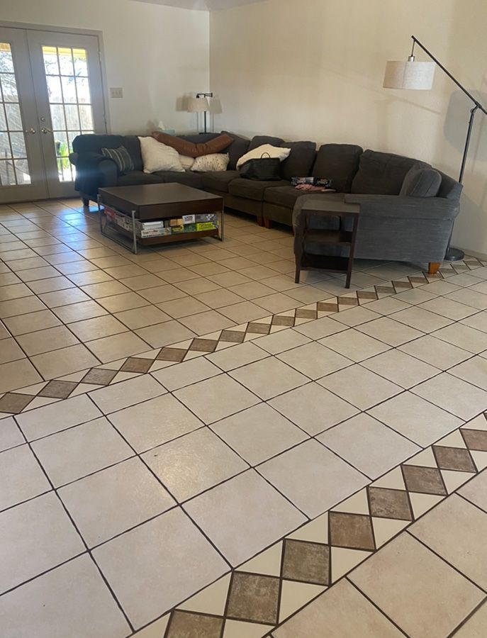 Living room with gray sectional sofa on tile floor. Border tiles in brown. Coffee table, side table.
