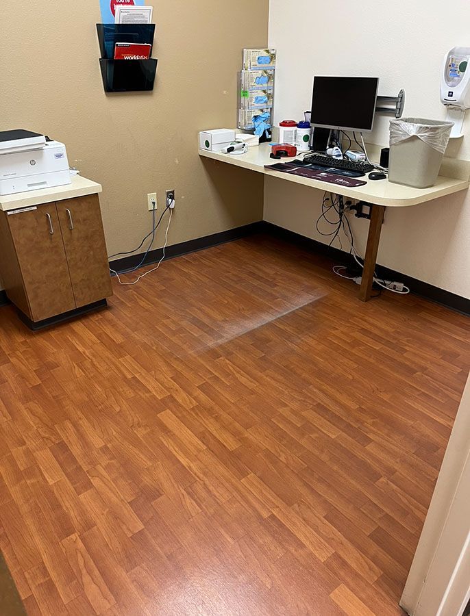 Medical office with desk, computer, cabinet, and brown flooring.